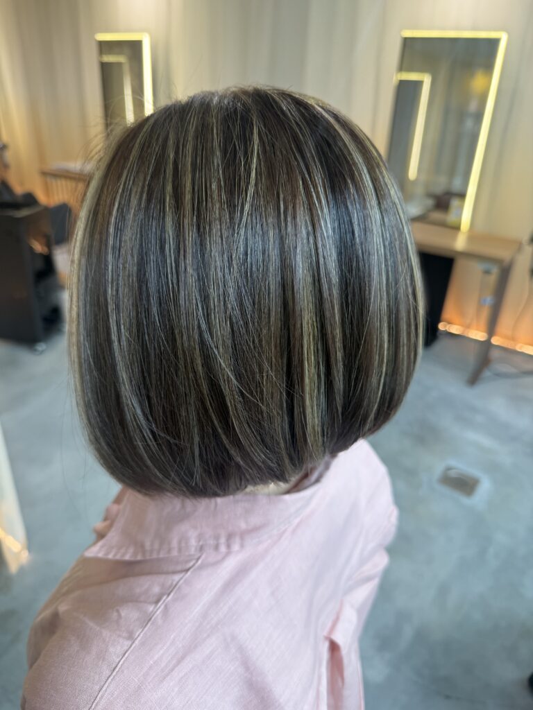 Grey blending highlights with ash beige tones on an angled bob at a Japanese Hair Salon Singapore. Low-damage Plex bleach, scalp cleansing spa, and HOYU treatment create natural grey blending with smooth, glossy hair.