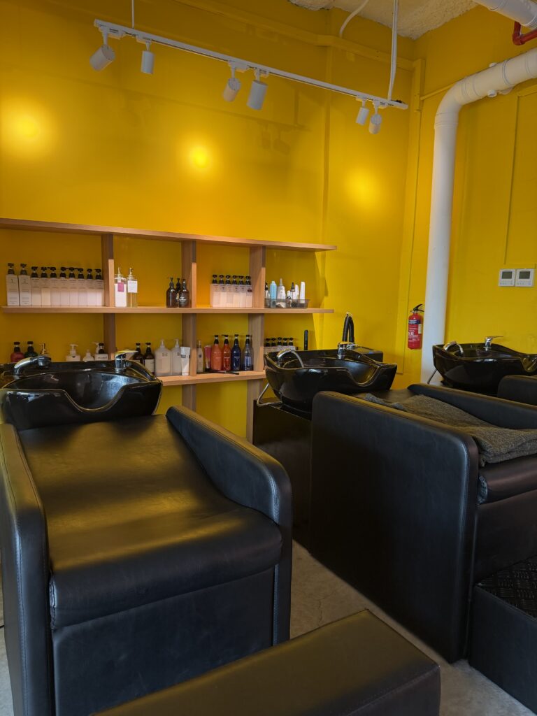 Clarke Quay MRT近く、Colors Japanese Hair Salon Singaporeのシャンプーラウンジ。長時間メニュー（グレイブレンディング／ブリーチ／縮毛矯正／カラー補正）でも快適に休めるリクライニングチェア設計です。