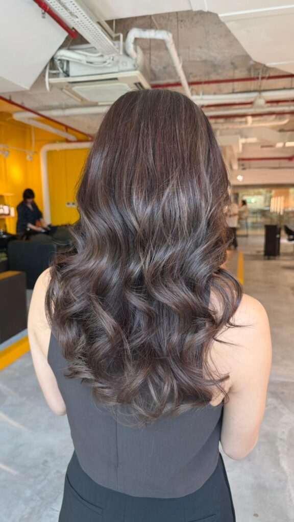 Long layered violet ash brown hairstyle with soft curls and elegant shine by Senior Stylist Sylvia at Colors Japanese Hair Salon Singapore.