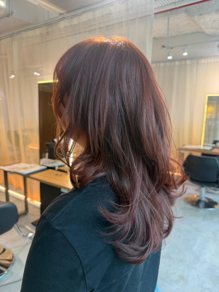 Medium layered pink red hair without bleach at Colors Japanese Hair Salon Singapore. Japanese hair salon Singapore specializing in low-damage plex color, medium layer cut, natural volume, and hair color for wavy hair near Clarke Quay.