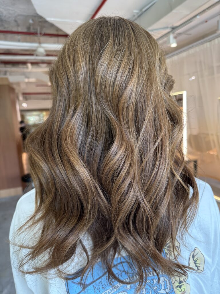 Long layered hair with a V-shaped back silhouette and bright honey brown grey coverage, designed to keep movement, shine and a softer regrowth line at a Japanese hair salon in Singapore.