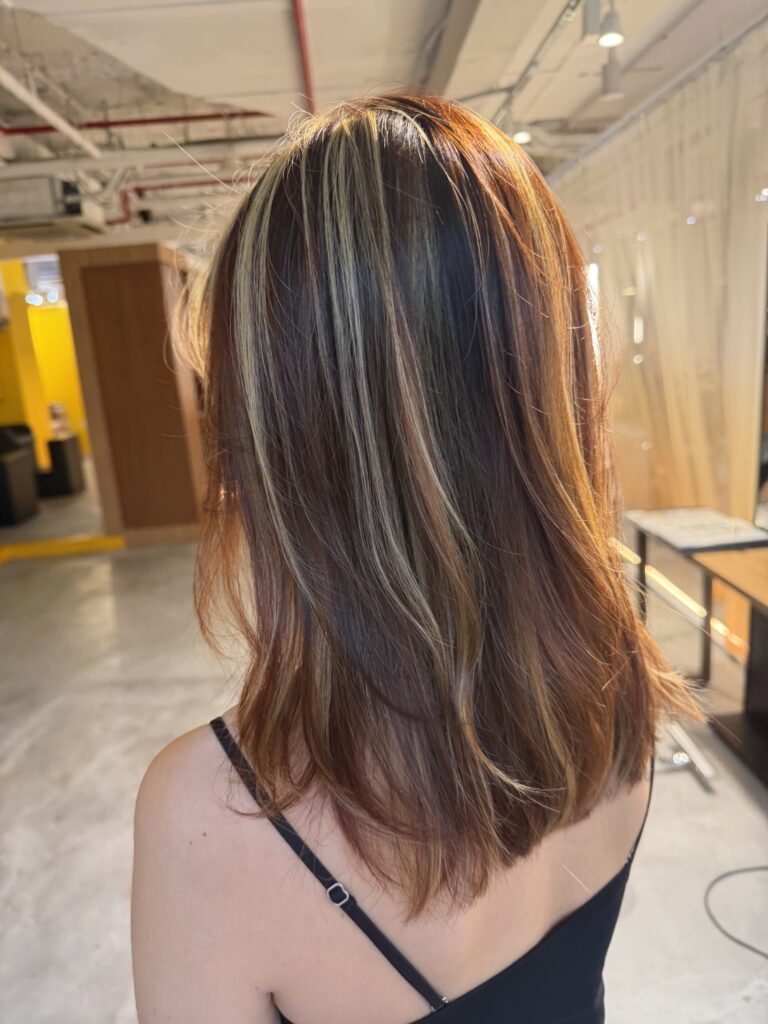 Medium layered hair with yellow blonde and dark copper highlights, created with Plex-supported color and bleach highlights in Singapore