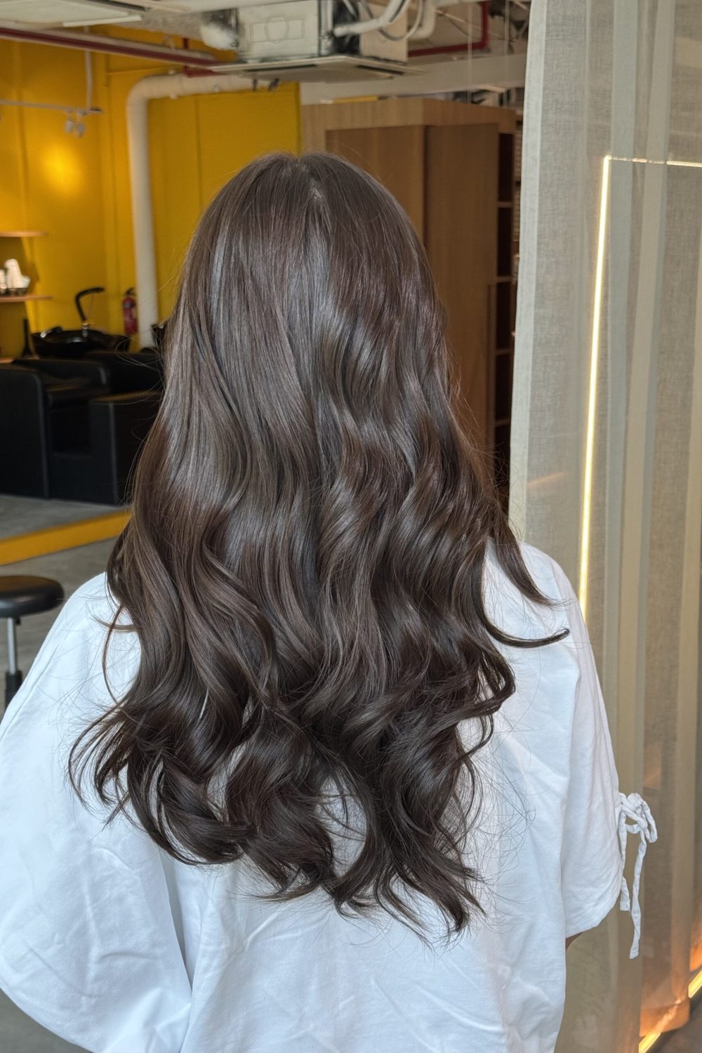 Long ash brown hair color on naturally dark hair with a soft root gradient and curled finish at a Japanese hair salon in Singapore.