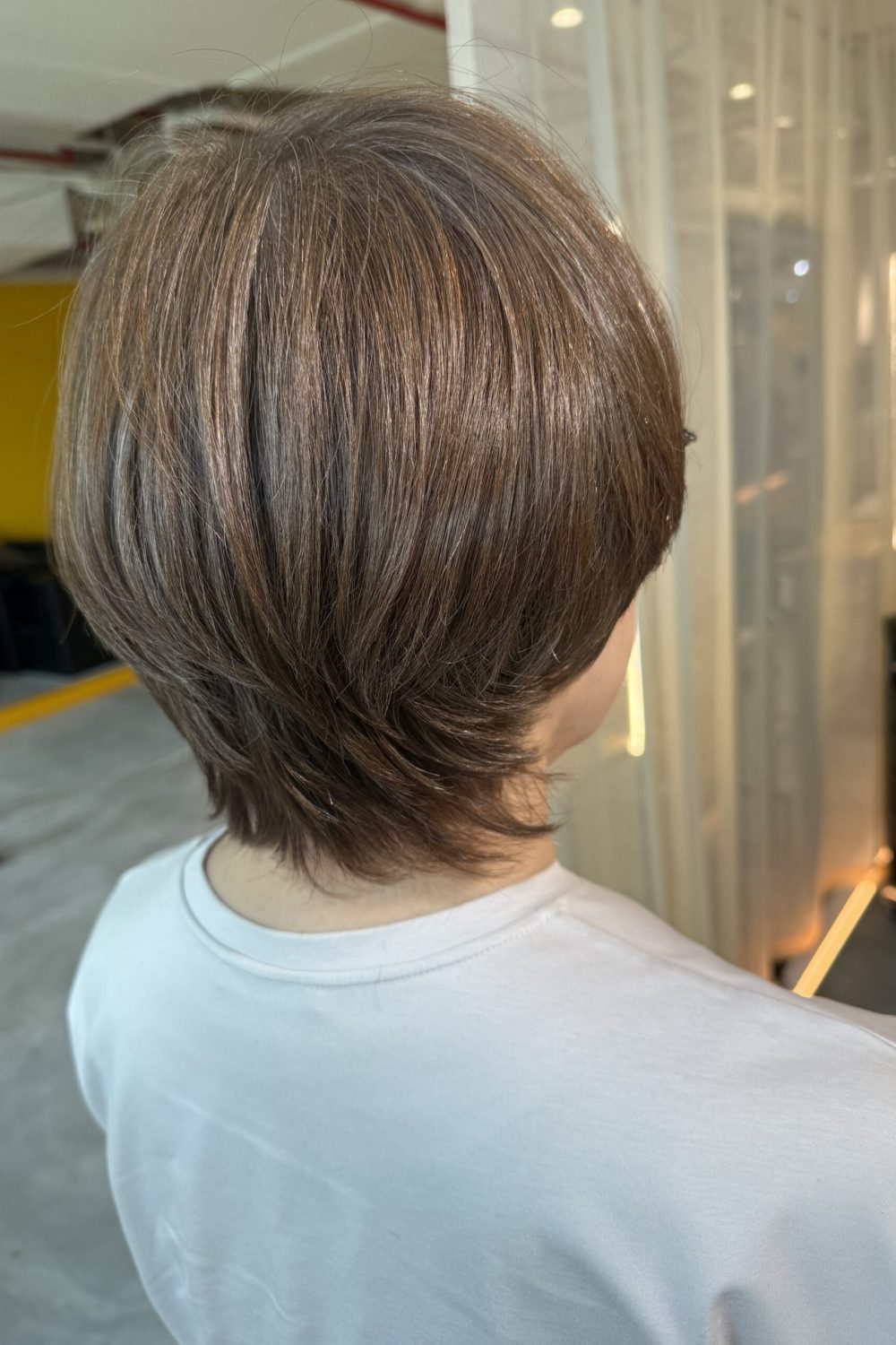 Short layered haircut with bright grey coverage in warm beige brown at a Japanese Hair Salon Singapore, featuring natural volume, longer nape design, and low-damage Plex hair color for seamless grey blending.